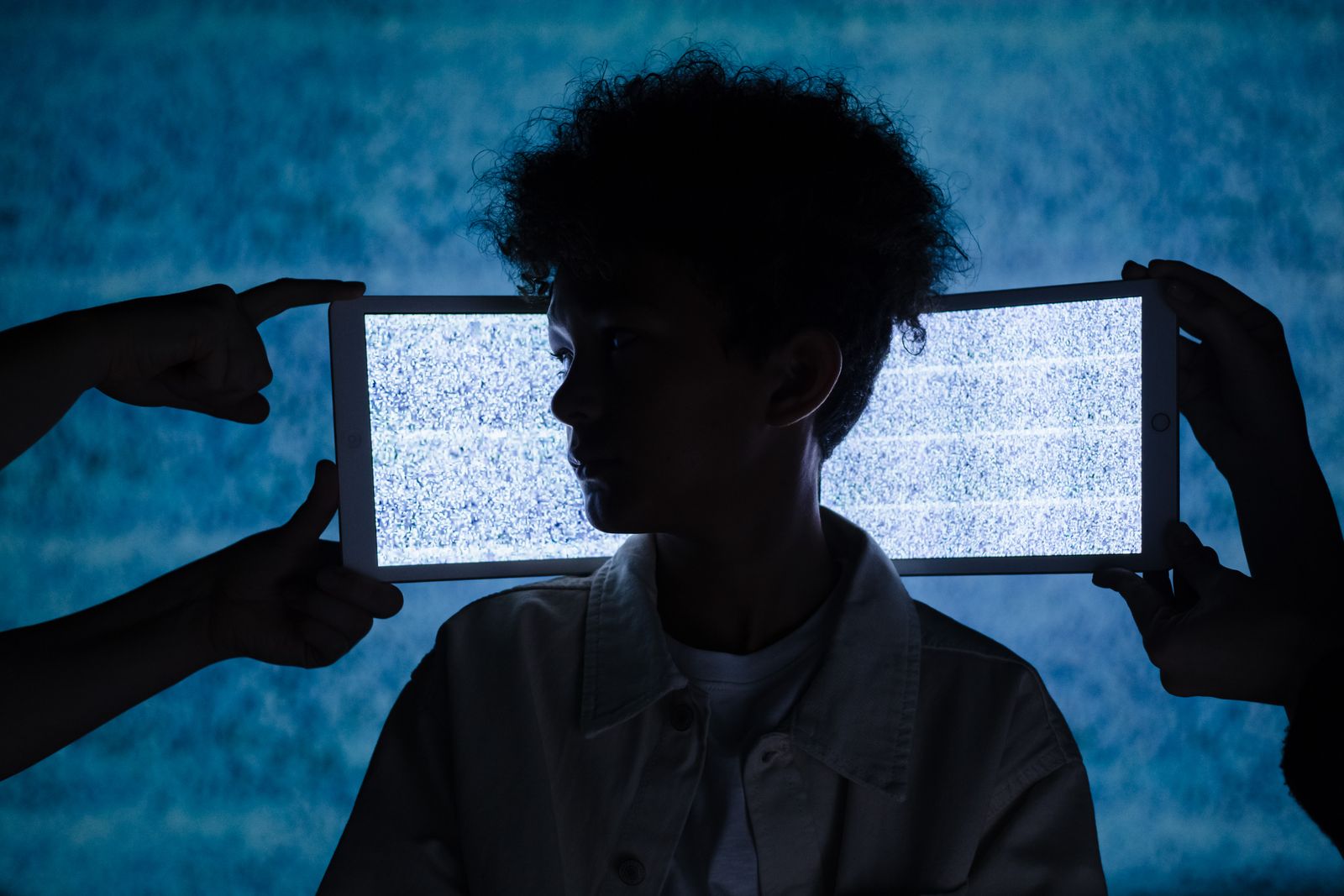 Photo artistique de la silhouette d'un enfant encadrée par des tablettes numériques affichant du statique, explorant la 